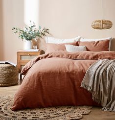 a bed with an orange comforter in a bedroom next to a plant and rug