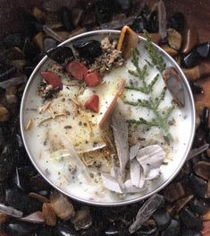 a metal bowl filled with lots of food on top of rocks and dirt covered ground