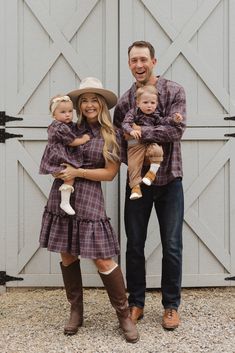 a man and woman are holding two small children in front of a barn door with their arms around each other