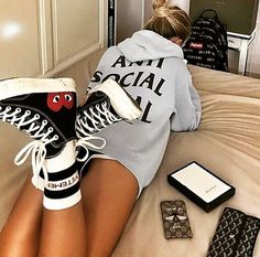 a woman sitting on top of a bed wearing black and white converse sneakers with eyes drawn on them