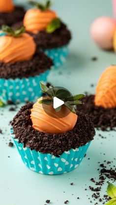 three cupcakes with chocolate frosting and orange icing on blue paper wrappers