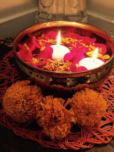 two candles in a bowl with flowers on the floor next to it and some rocks