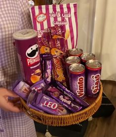 a woman is holding a basket full of snacks and candy bars on the table in front of her