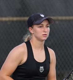 a woman holding a tennis racquet on top of a tennis court with a chain link fence in the background