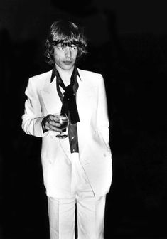 a man in a white suit and tie holding a wine glass with his right hand