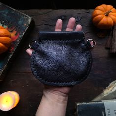 a hand holding a small black leather pouch next to some candles and pumpkins in the background