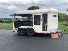 a white trailer parked in a parking lot next to a tree and grass covered field