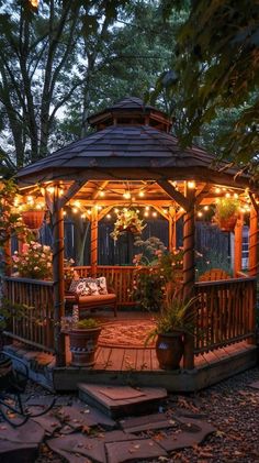 a wooden gazebo with lights on it in the middle of some trees and plants