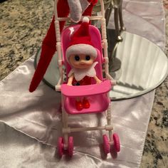 an elf doll sitting in a pink baby stroller on a table next to a christmas tree