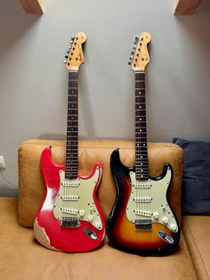 two guitars are sitting side by side on a couch, one is red and the other is black