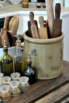 an assortment of kitchen utensils in a bucket on a table with jars and spoons