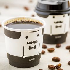 two coffee cups sitting next to each other on top of a white table covered in nuts