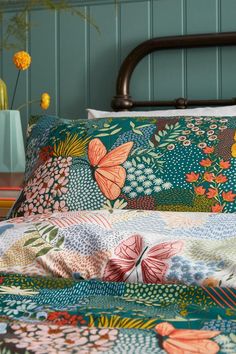 a bed covered in colorfully colored sheets and pillows with flowers on them next to a green wall