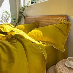 a bed covered in yellow sheets and pillows next to a wicker basket on the floor