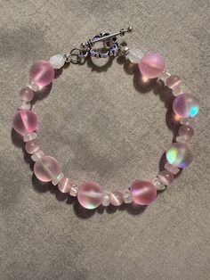 Made with Pink Mermaid Glass style beads. Moonstones and pink cat's eye beads in between bigger beads. It was wire and has a silver color toggle. I added an extender. It is now 9 inches long with the extender. Pink Wire Wrapped Beaded Bracelets With Round Beads, Handmade Pink Moonstone Jewelry, Handmade Pink Glass Bracelets, Pink Beaded Glass Bracelets, Pink Glass Beaded Bracelets, Pink Czech Glass Bracelets With Spacer Beads, Mermaid Glass, Pink Mermaid, Glass Style