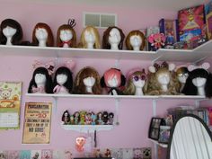 many wigs are lined up on the shelves in a girls'room, and there is also a mirror