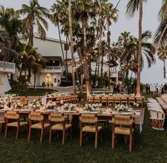 an outdoor dining area with tables and chairs set up in front of palm trees at dusk