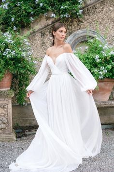 a woman wearing a white dress standing in front of flowers