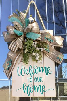 a welcome to our home sign hanging on the side of a building with flowers and ribbons