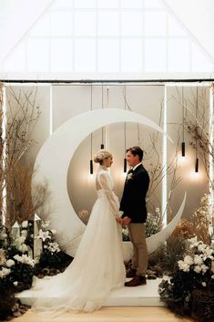 a bride and groom standing next to each other in front of a wall decorated with flowers