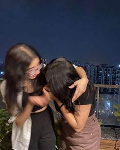 two young women are hugging each other on a balcony overlooking the city lights at night