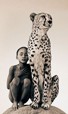 a woman sitting on top of a rock with a cheetah standing next to her