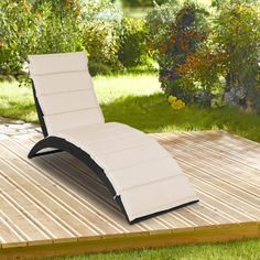 an outdoor lounge chair sitting on top of a wooden deck in front of some bushes