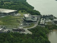 an aerial view of a large building in the middle of some trees and water with a body of water behind it