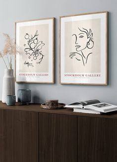 two framed art prints on the wall above a wooden cabinet with vases and books