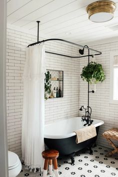 a black and white tiled bathroom with a claw foot bathtub, shower curtain, potted plant and stool