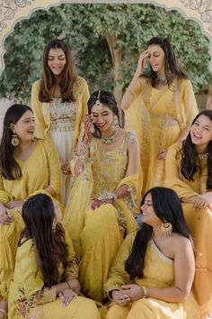 a group of women sitting next to each other wearing yellow dresses and smiling for the camera