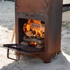 a fire burning inside of a metal oven on top of sandy beach next to water