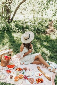 a woman sitting on a blanket in the grass eating food and drinking from a bottle