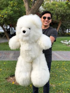 a man standing next to a large white teddy bear on top of a lush green field