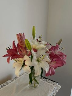 a vase filled with pink and white flowers on top of a lace table cloth next to a window