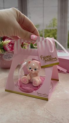 a hand holding a small pink teddy bear in a gift bag with its lid open