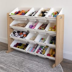 a wooden shelf with bins filled with toys on top of carpeted floor next to wall