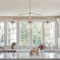 a kitchen island with three lights hanging from it's ceiling and windows in the background