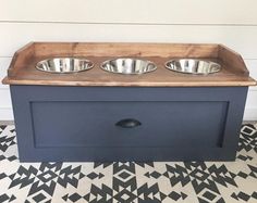 two metal bowls sit on top of a wooden box with black and white tile flooring