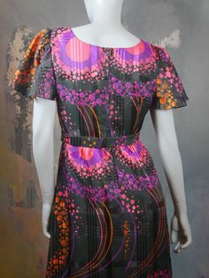 This 1970s mod dress has a stunningly vibrant purple, pink, and orange effervescent abstract polka dot pattern on a black satin sheen background. The dress has a round neckline and short sheer puff sleeves, and a fitted waistline with a matching belt gives way to an A-line drop to the midi-length hemline. The dress is lined in a black satin viscose-nylon fabric, and closes in the back with an 18.5-inch zipper. Bust = 40 inches (101cm) Shoulders = 16.5 inches (41.91cm) Waist = 32 inches (81.28cm) Fitted Mod Dress With Vintage Print, Mod Fitted Dress With Vintage Print, Vintage Purple A-line Dress, Retro Colorful Dresses With Vibrant Print, Colorful Retro Dresses With Vibrant Print, Retro Dresses With Vibrant Print, Retro Multicolor Lined Mini Dress, Multicolor Vintage Print Dress, 1970s Fitted Purple Dress