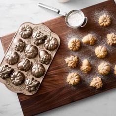 a wooden cutting board topped with cookies next to a cookie pan filled with mini pumpkins