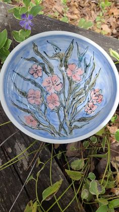 a bowl with flowers painted on it sitting on a wooden table next to leaves and plants