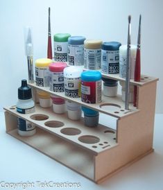 an assortment of paint and acrylic paints on a wooden holder with holes in it