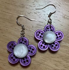 two purple and white flower shaped earrings sitting on top of a wooden table next to each other