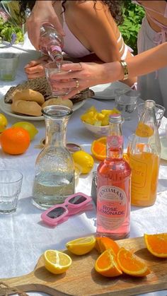 two women at a table with oranges, lemons and bottles of alcohol on it