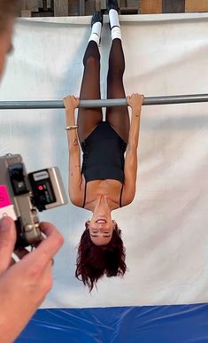 a woman is upside down in the air while holding a cell phone up to her face