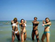 four women standing in the ocean with their arms around each other and wearing bikinis