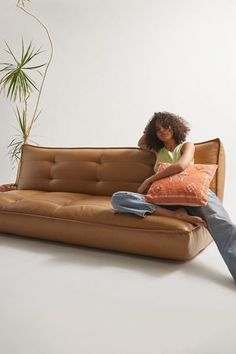 a woman sitting on top of a brown couch next to a potted plant