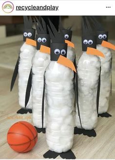 three penguins made out of plastic bottles sitting next to a basketball