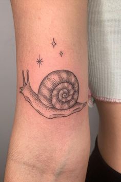 a small snail tattoo on the side of a woman's leg, with stars above it